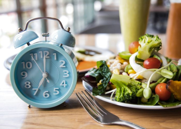 alarm clock next to a healthy plate of food indicating when you may eat if intermittent fasting