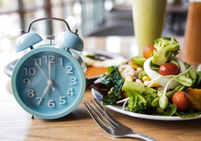 alarm clock next to a healthy plate of food indicating when you may eat if intermittent fasting