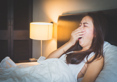 woman yawning in bed at night - what causes insomnia | Perpetual Wellbeing